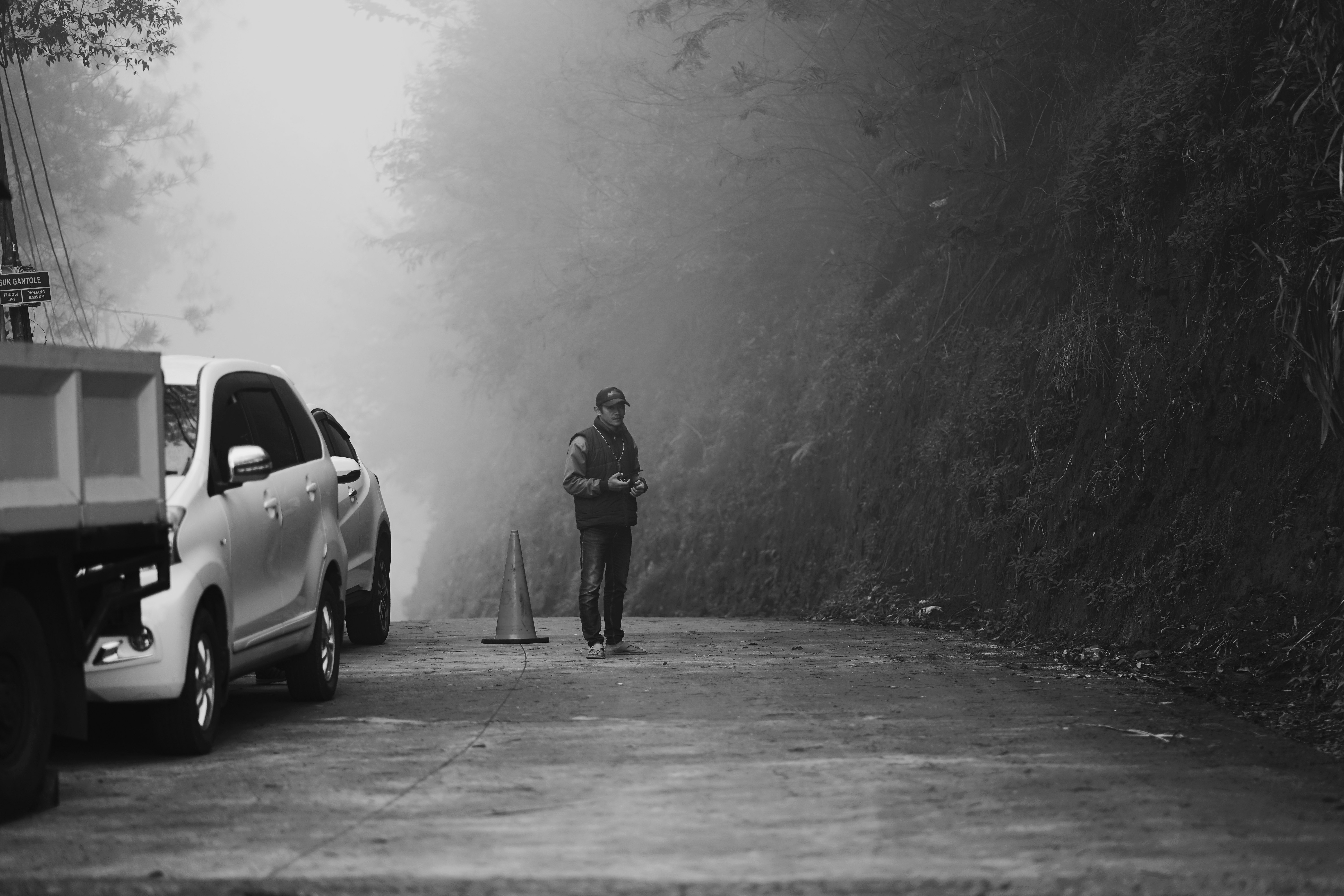 grayscale photo of man standing beside car